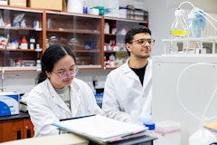 Two students working in lab, one male/one female wearing lab coats and glasses