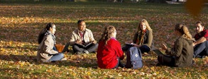 Photo of a group of six students sitting on Johnston Green in the fall, leaves all around them. 