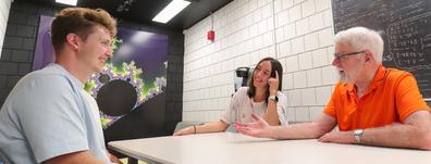 two students and a professor sit at a table and discuss mathematics