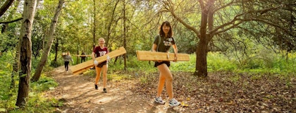 two people carrying wood planks along forested trail