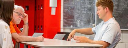 Three students engaging in discussion in a classroom.