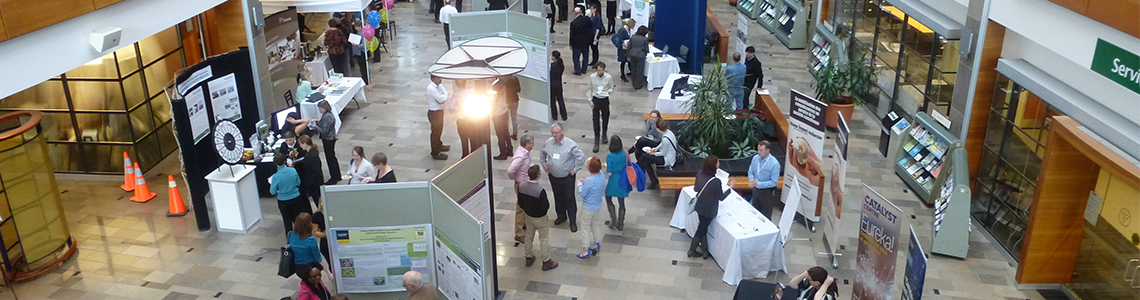 Image taken from above of people at an event inside a building visiting booths and reading scientific posters 
