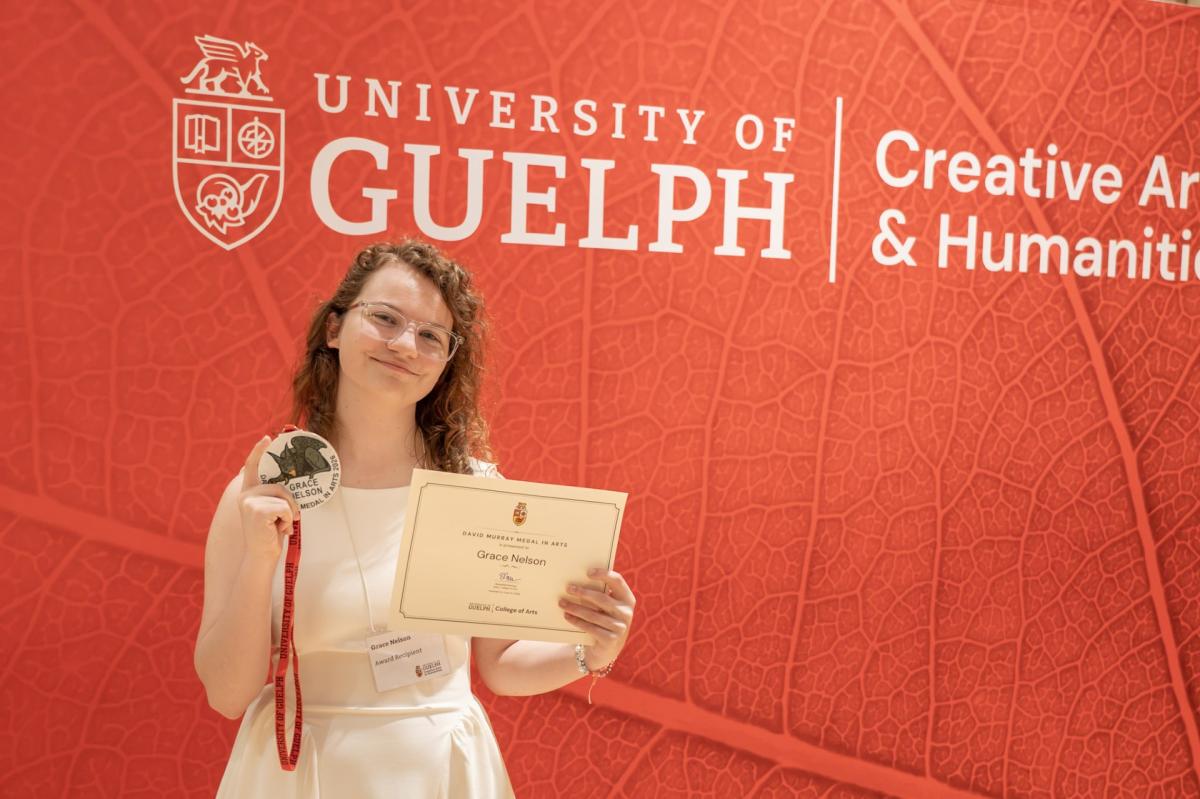 Grace Nelson holding the David Murray Medal in Arts and the accompanying award certificate at the June 2026 College of Arts Convocation Awards Ceremony in the MacKinnon Auditorium in the Arts Research Centre at the University of Guelph.