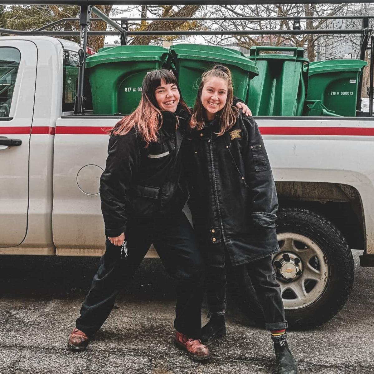 two student employees pose with the composting vehicle