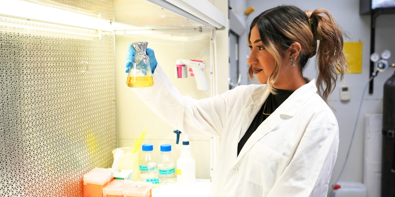 Simran Kaur holds a beaker in a fume hood
