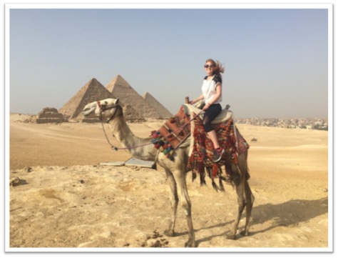 Photo of student on a camel in front of pyramids
