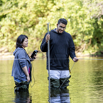 2 students standing in a river with a stream gauging device