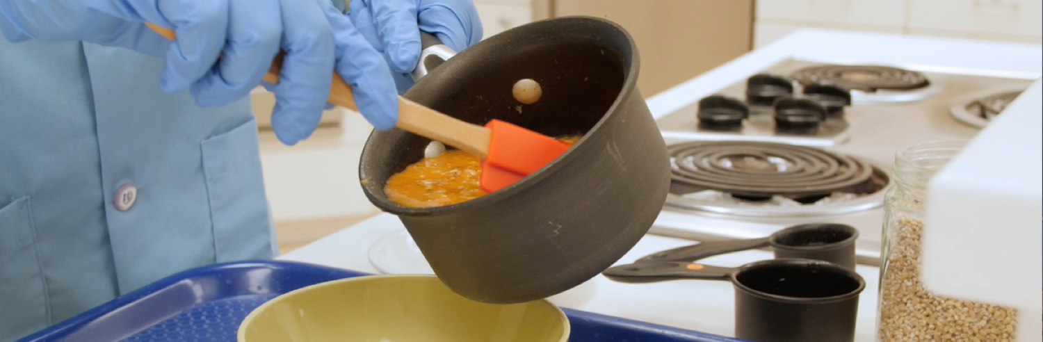 Student pouring lentil soup from a saucepan into a bowl.