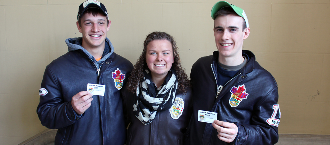 Two male and one female student stand together all wearing matching leather jackets and holding up membership cards