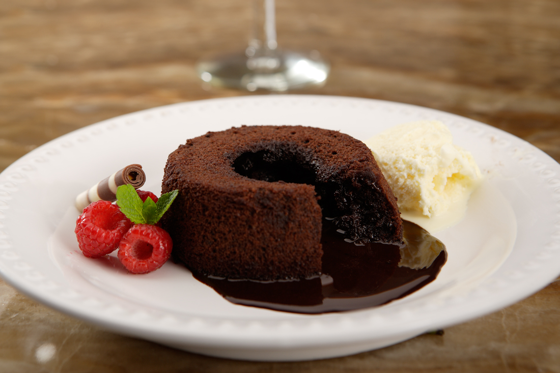 Chocolate cake, with chocolate syrup oozing from centre, on white plate