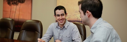 Two people talk to each other around a board room table.