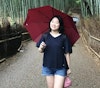 Shing-Tian stands with umbrella on a path between rows of bamboo