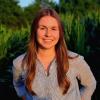 Kelly smiling in dress shirt standing in front of green corn field