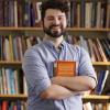 Matthew Hernandez holds a philosophy book while standing in front of a book shelf.