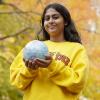 Prakrithi Monteiro wears a yellow University of Guelph sweatshirt and cradles a small globe in her hands.