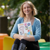 Emma Biffi sits holder a laptop covered in stickers on rainbow benches.