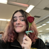 Zoe holds a rose next to her face while smiling at the camera.
