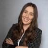Close-up portrait of Emily Farrel smiling, dressed in a blazer, with a neutral grey background.