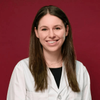 Close-up portrait of Maya smiling, dressed in a  white lab coat, with a red background.