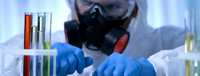 A student in a lab coat and mask conducting an experiment with a test tube.