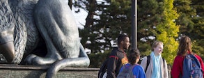 Photo of a group of five students talking to each other in front of the Gryphon statue. 