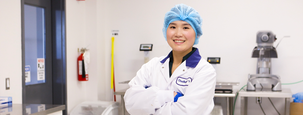 aleana standing in a food lab, arms folded, wearing a lab coat and hair net