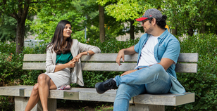 Two University of Guelph Students sitting on a bench4 at a distance from each other, chatting.