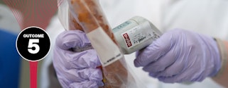 Close-up of a lab technician’s nitrile-gloved hands holding a small scanner to a plastic-wrapped coil of meat