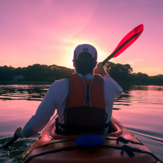 A man paddling a kayak on calm waters during a sunset.