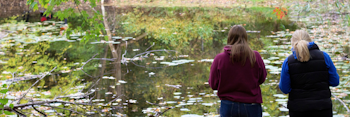 Two students standing next to a pond