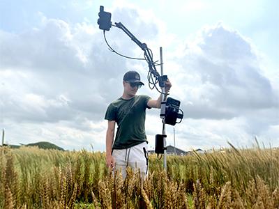 Riley McConachie holding equipment in a wheat field under a cloudy sky.