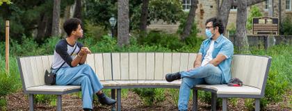 two University of Guelph students sitting on a bench at a distance from each other, chatting.