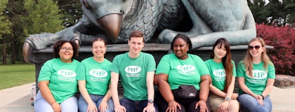 Students in Peer Helper T-shirts sitting in front of the Gryphon statue