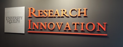 Metallic sign reading 'University of Guelph' on a gray wall, next to large, raised red letters spelling 'RESEARCH INNOVATION'