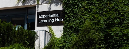 Sign reading "Experiential Learning Hub" on foliage-covered building