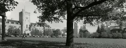 A black and white photo of a stone clock tower building surrounded by a grassy field and trees.