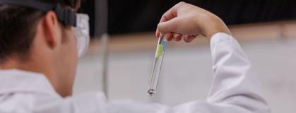 Student in lab gear analyzing a test tube.
