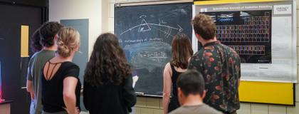 A group of students stand around a physics chalkboard at the university of guelph