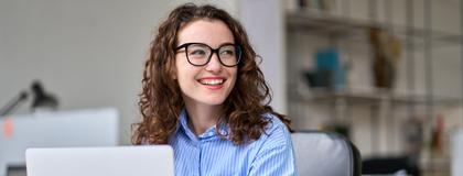 A professional smiles while working on computer and sitting in an office setting.