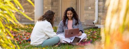 Two students sitting on grass and chatting outside the east residence