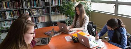 A group of students sitting around a table, working on their laptops in a collaborative study environment.