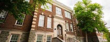 The front face of a red brick building with green trees around it