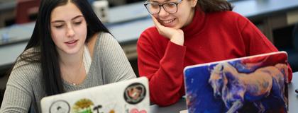 Two students look at their laptops, smiling.