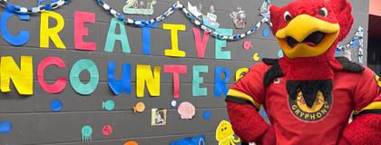 Image of Gryph in Thornborough building in front of Creative Encounters signage