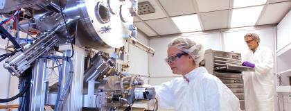 Two researchers working with equipment in a sterile lab wearing ppe