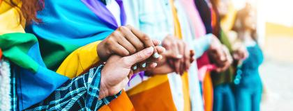 People stand in a line holding hands with pride flag