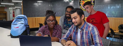 a photo of students point and looking at a laptop