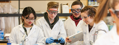 students inspecting specimen in a lab, wearing coats