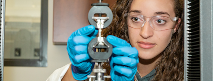 Female student wearing blue medical gloves, placing a material in a tensile tester