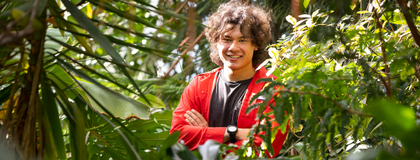 a student in a greenhouse smiling and crossing his arms